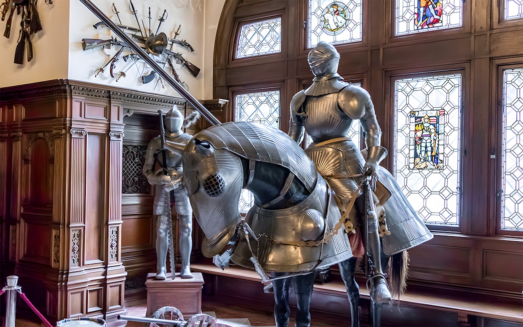Knight armor display inside Peles Castle with stained glass windows.