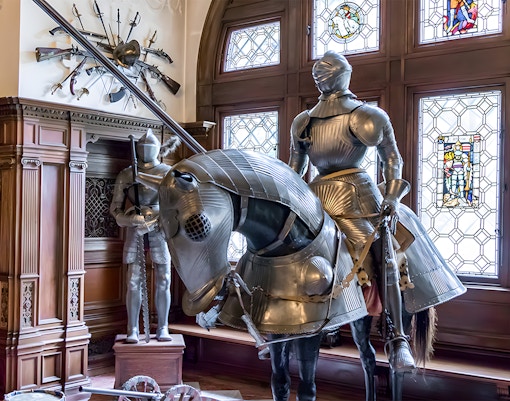 Knight armor display inside Peles Castle with stained glass windows.