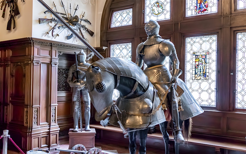 Knight armor display inside Peles Castle with stained glass windows.