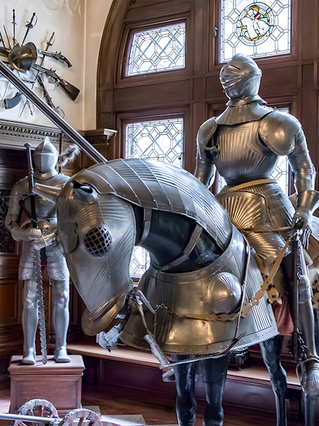 Knight armor display inside Peles Castle with stained glass windows.
