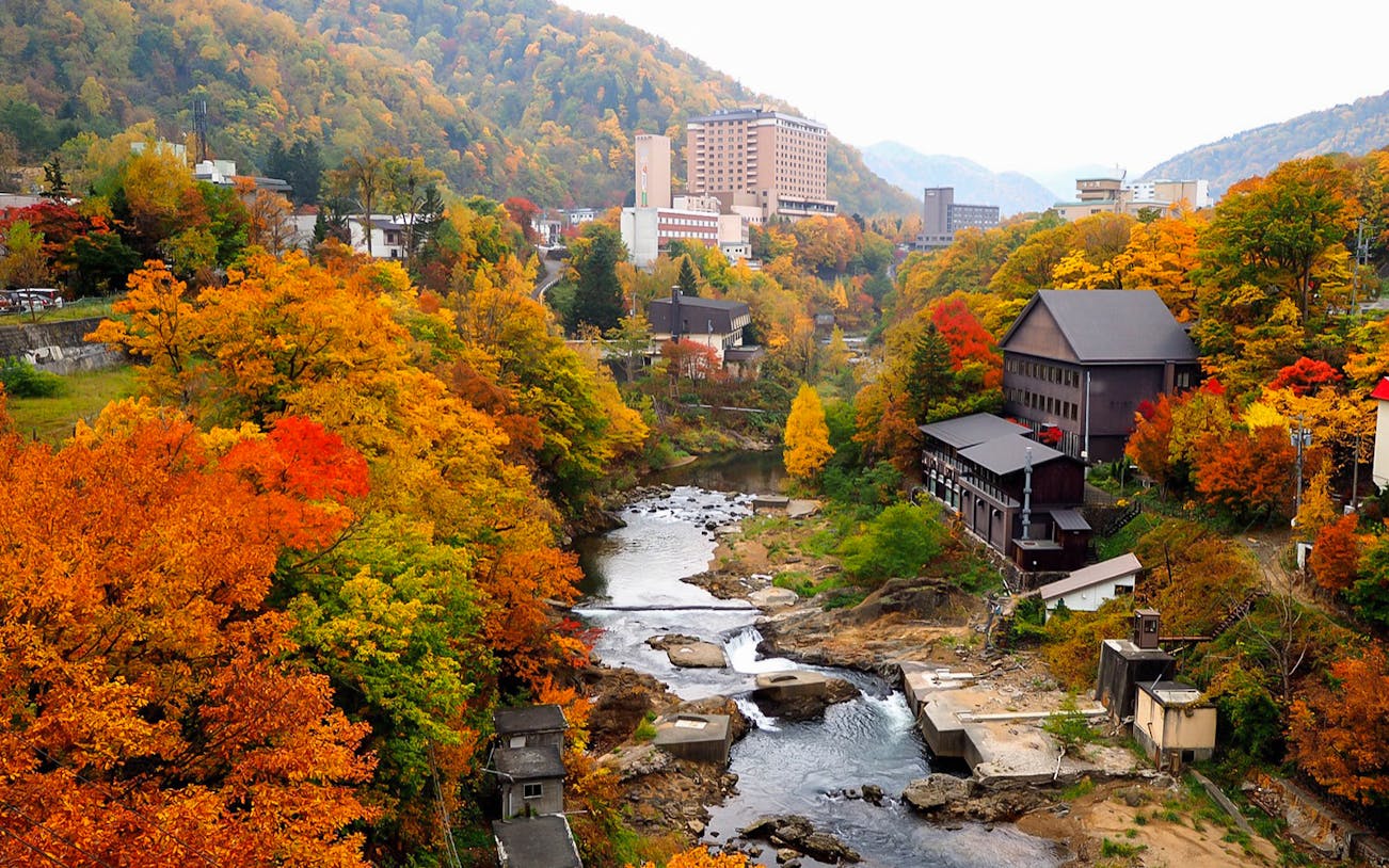Jozankei Mori No Uta Onsen surrounded by vibrant autumn foliage and a flowing river.