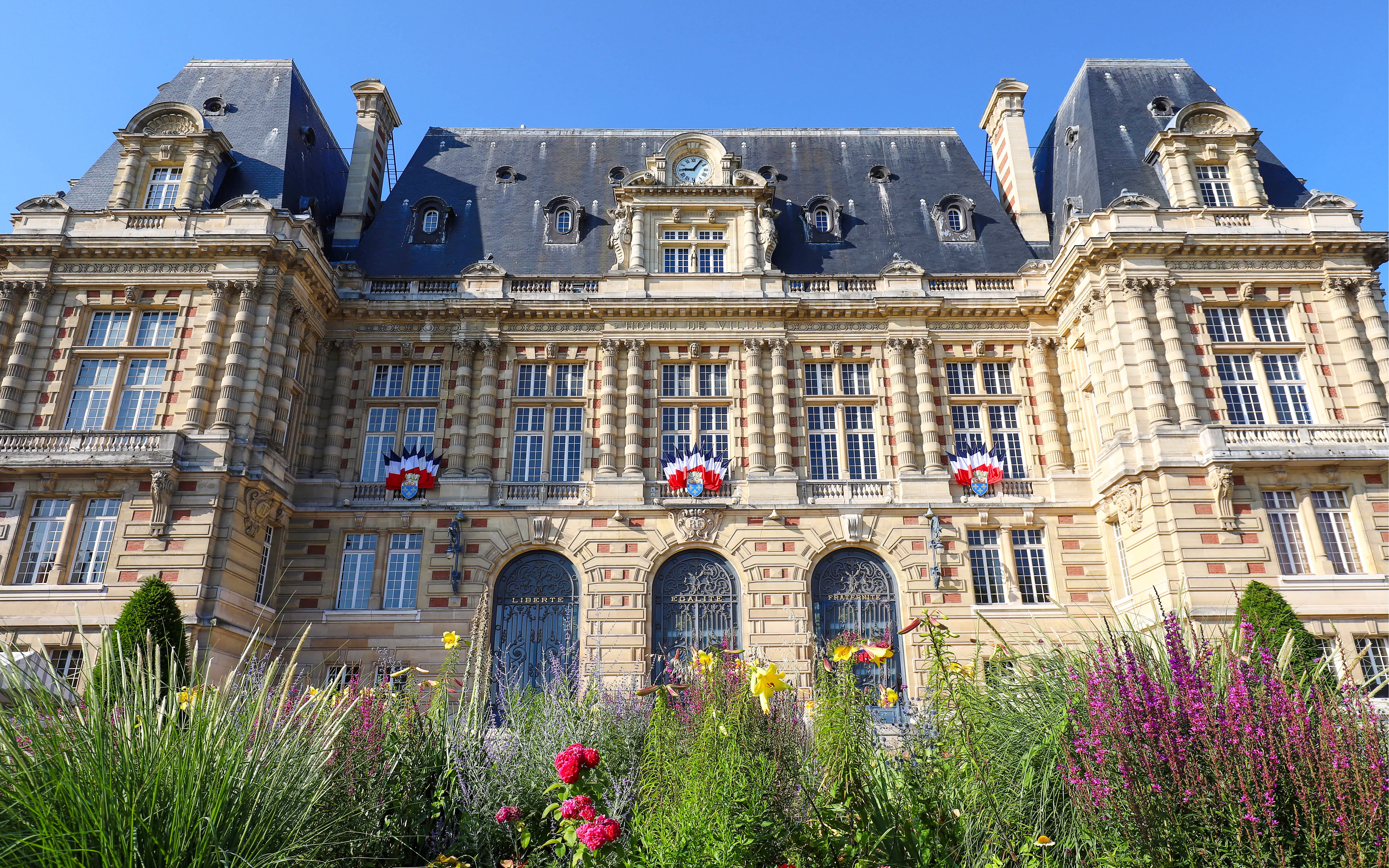 Versailles Town Hall facade with French flags and garden in foreground.