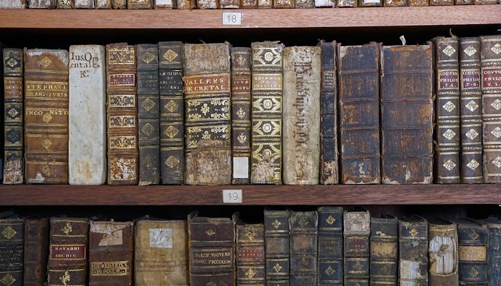 Bookshelf in library with antique medieval books displayed.