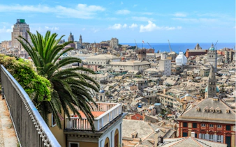 Genoa cityscape with historic buildings and palm trees, view from a terrace overlooking the sea.
