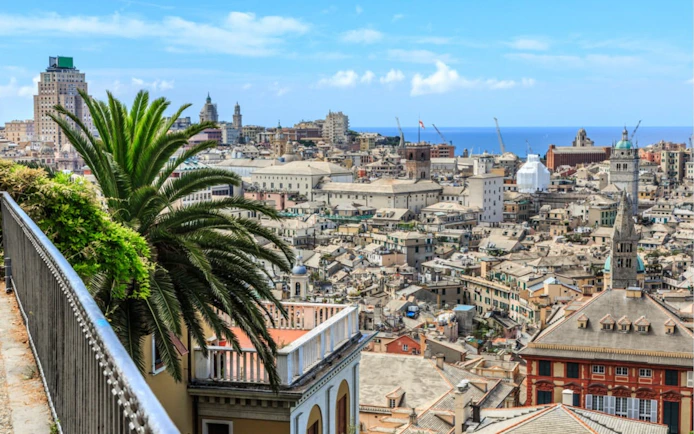 Genoa cityscape with historic buildings and palm trees, view from a terrace overlooking the sea.
