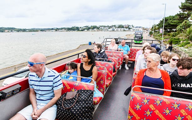 Tourists on Bournemouth hop-on hop-off bus enjoying coastal views.