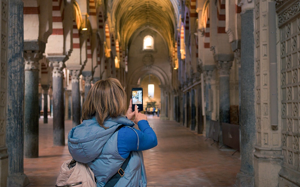 Visitor photographing arches inside Cordoba Mosque-Cathedral during guided tour.