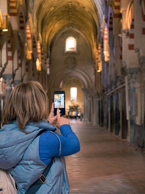 Visitor photographing arches inside Cordoba Mosque-Cathedral during guided tour.