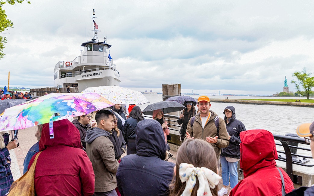 Guide speaking to visitors near Statue of Liberty ferry in New York.