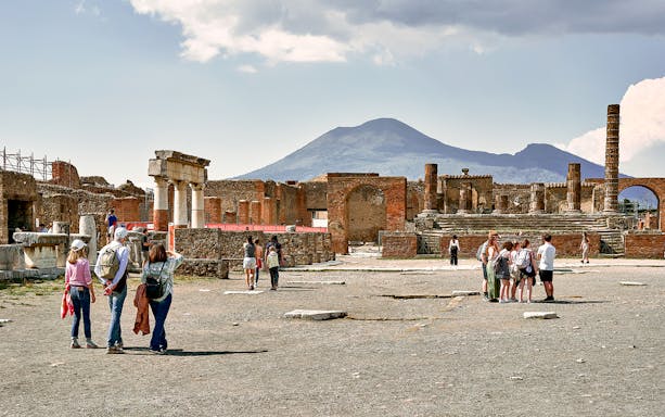 Tourists exploring ancient ruins of Pompeii with Mount Vesuvius in the background.