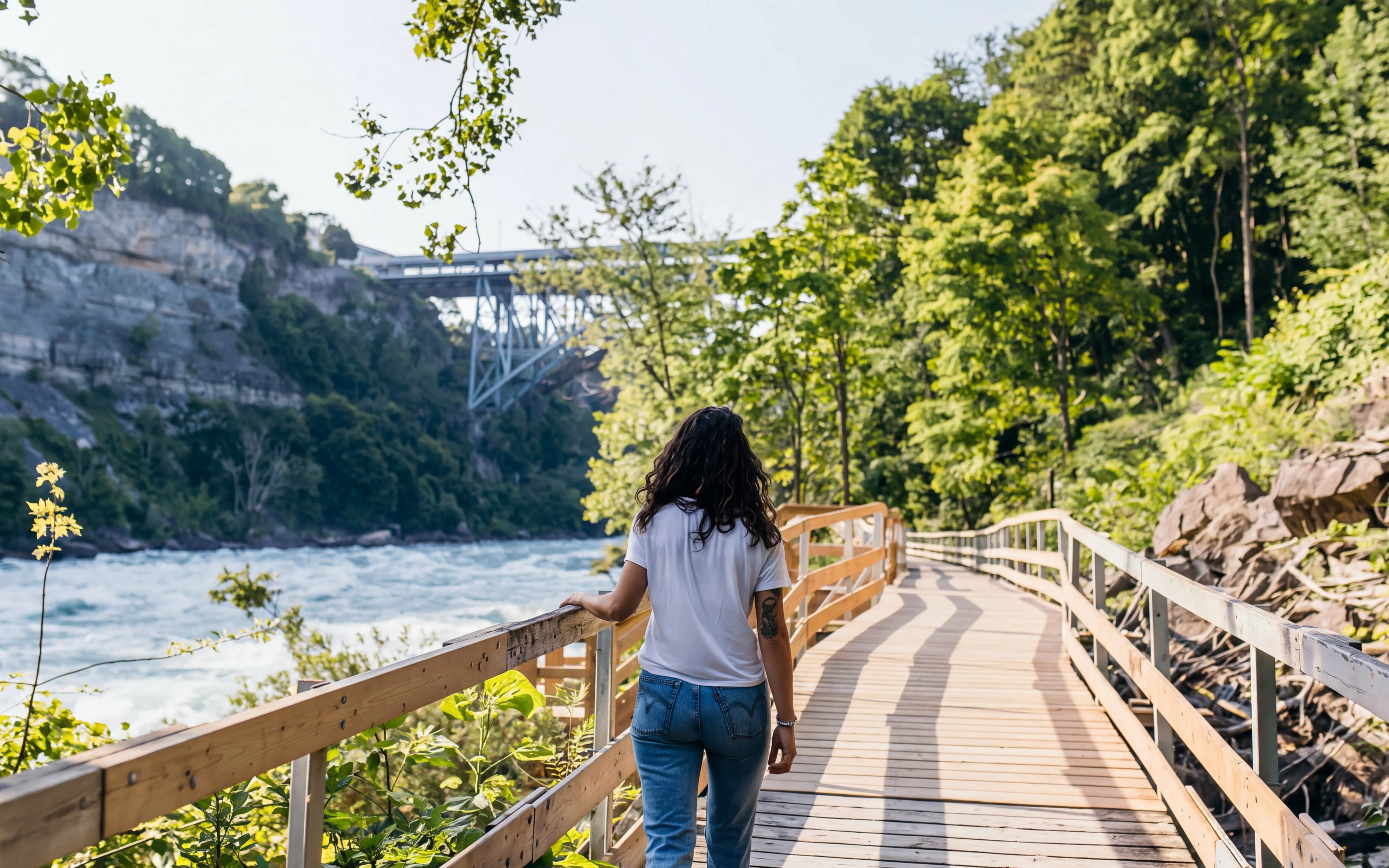 Person walking along the White Water Walk boardwalk in Niagara Falls, surrounded by trees and river.