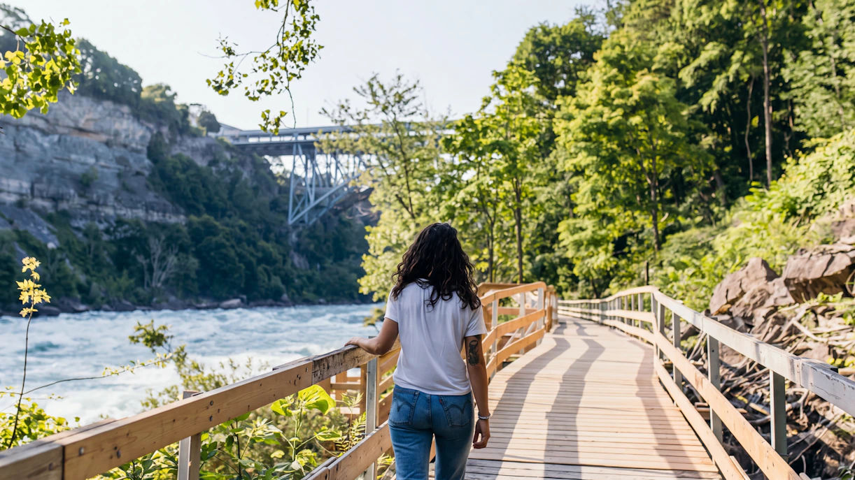Person walking along the White Water Walk boardwalk in Niagara Falls, surrounded by trees and river.