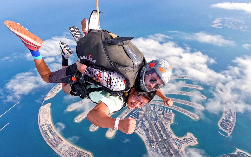 Skydivers over Palm Jumeirah, Dubai, with aerial view of the island below.