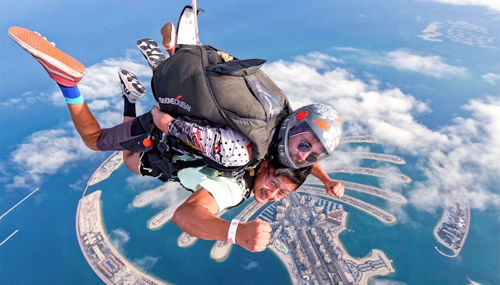 Skydivers over Palm Jumeirah, Dubai, with aerial view of the island below.