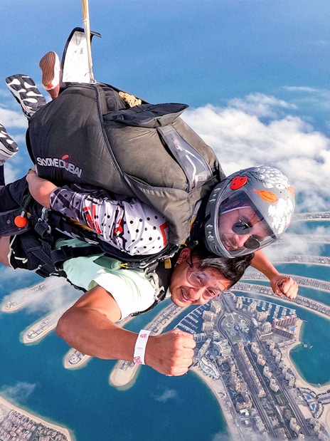 Skydivers over Palm Jumeirah, Dubai, with aerial view of the island below.