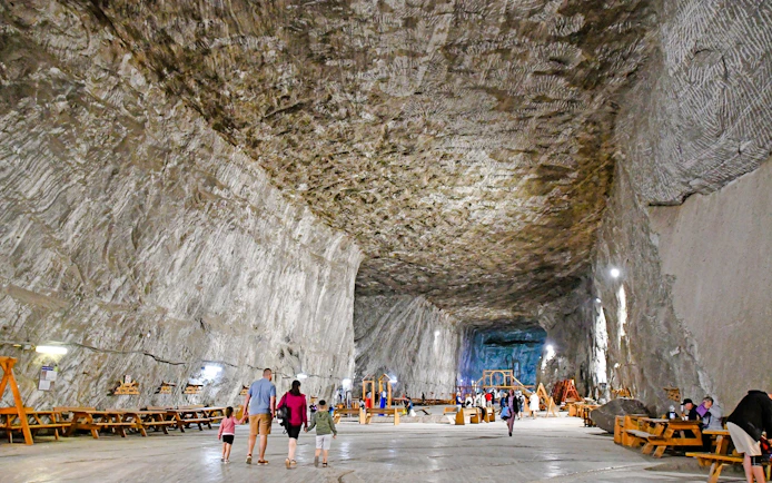 Guests walking inside Slanic Salt Mine, Romania, with large salt walls and benches.