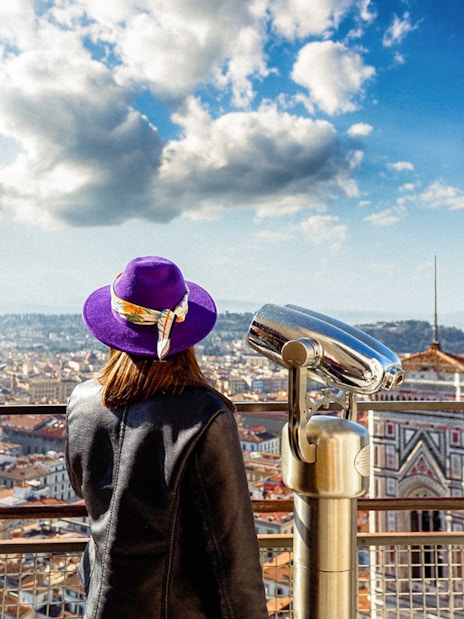 Girl viewing Florence from cathedral dome with cityscape and telescope.