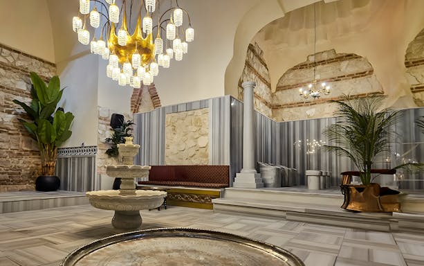 Gedikpasa Historical Hammam interior with ornate chandelier and marble fountain.
