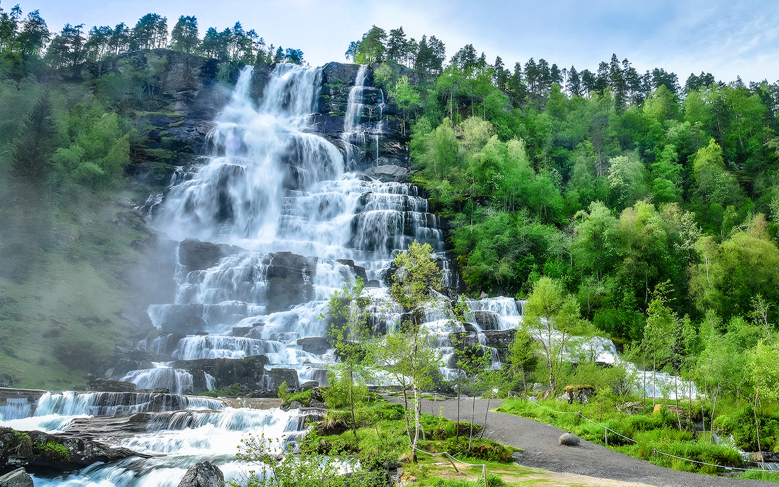 Tvindefossen waterfall cascading down a rocky cliff surrounded by lush greenery in Norway.