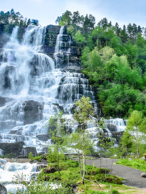 Tvindefossen waterfall cascading down a rocky cliff surrounded by lush greenery in Norway.