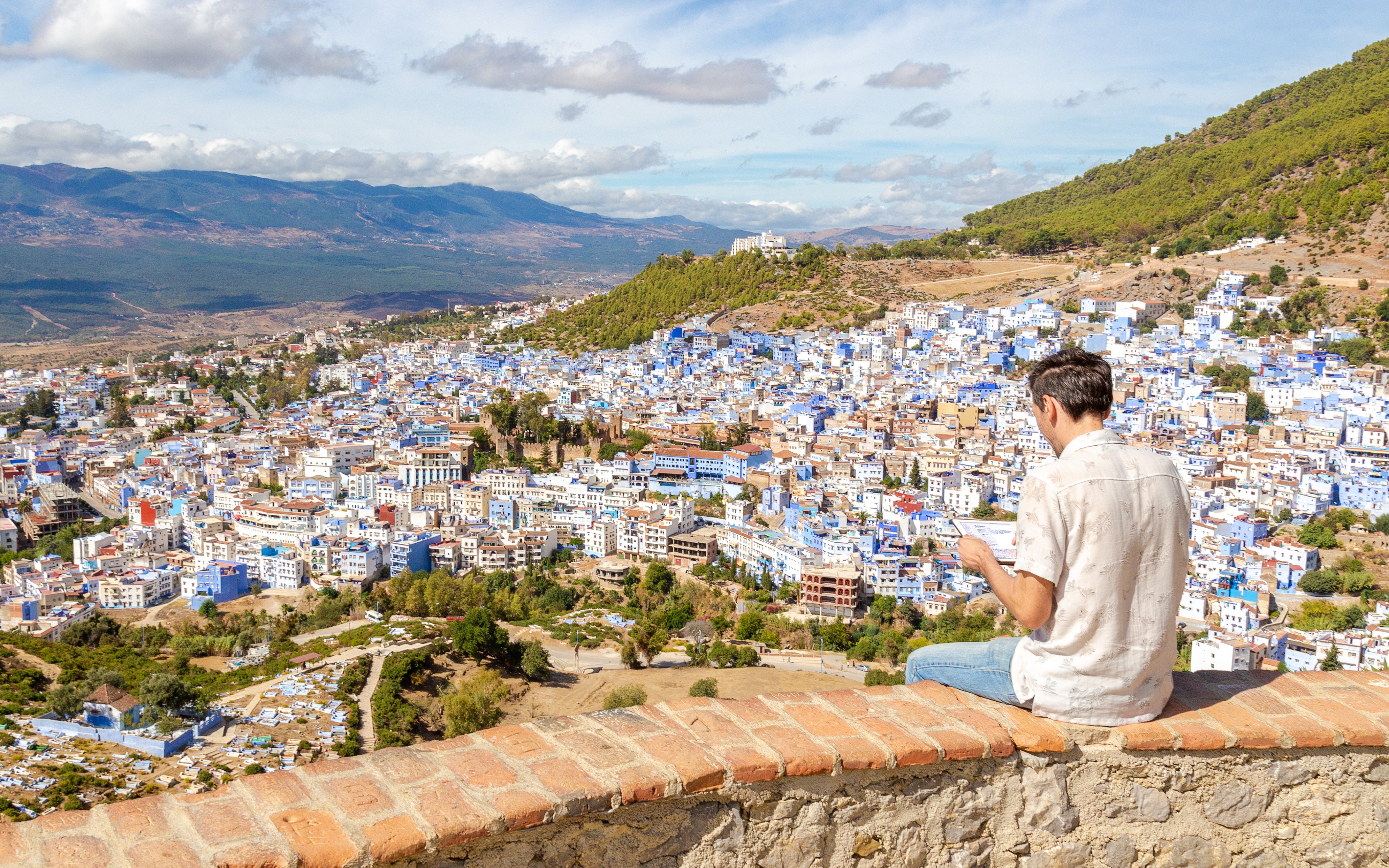 Man sitting on a wall overlooking the blue buildings of Chefchaouen, Morocco.