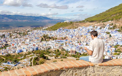 Man sitting on a wall overlooking the blue buildings of Chefchaouen, Morocco.