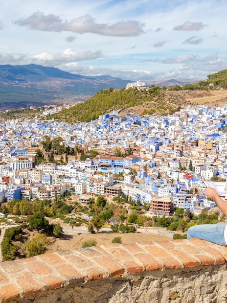 Man sitting on a wall overlooking the blue buildings of Chefchaouen, Morocco.