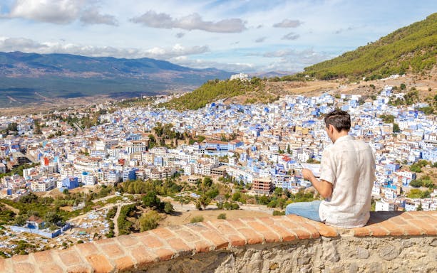 Man sitting on a wall overlooking the blue buildings of Chefchaouen, Morocco.