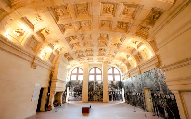 Chambord Castle interior with ornate ceiling and large arched windows.