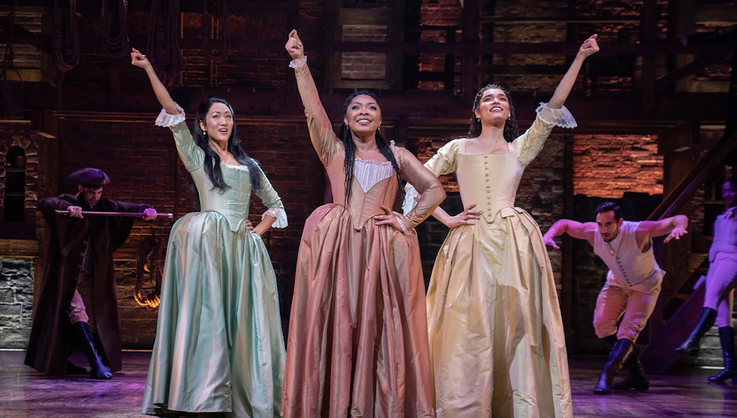 Performers in period costumes on stage during a scene from the musical Hamilton.