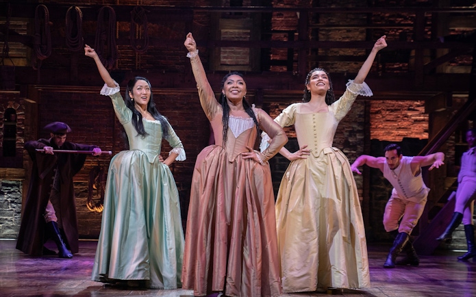 Performers in period costumes on stage during a scene from the musical Hamilton.