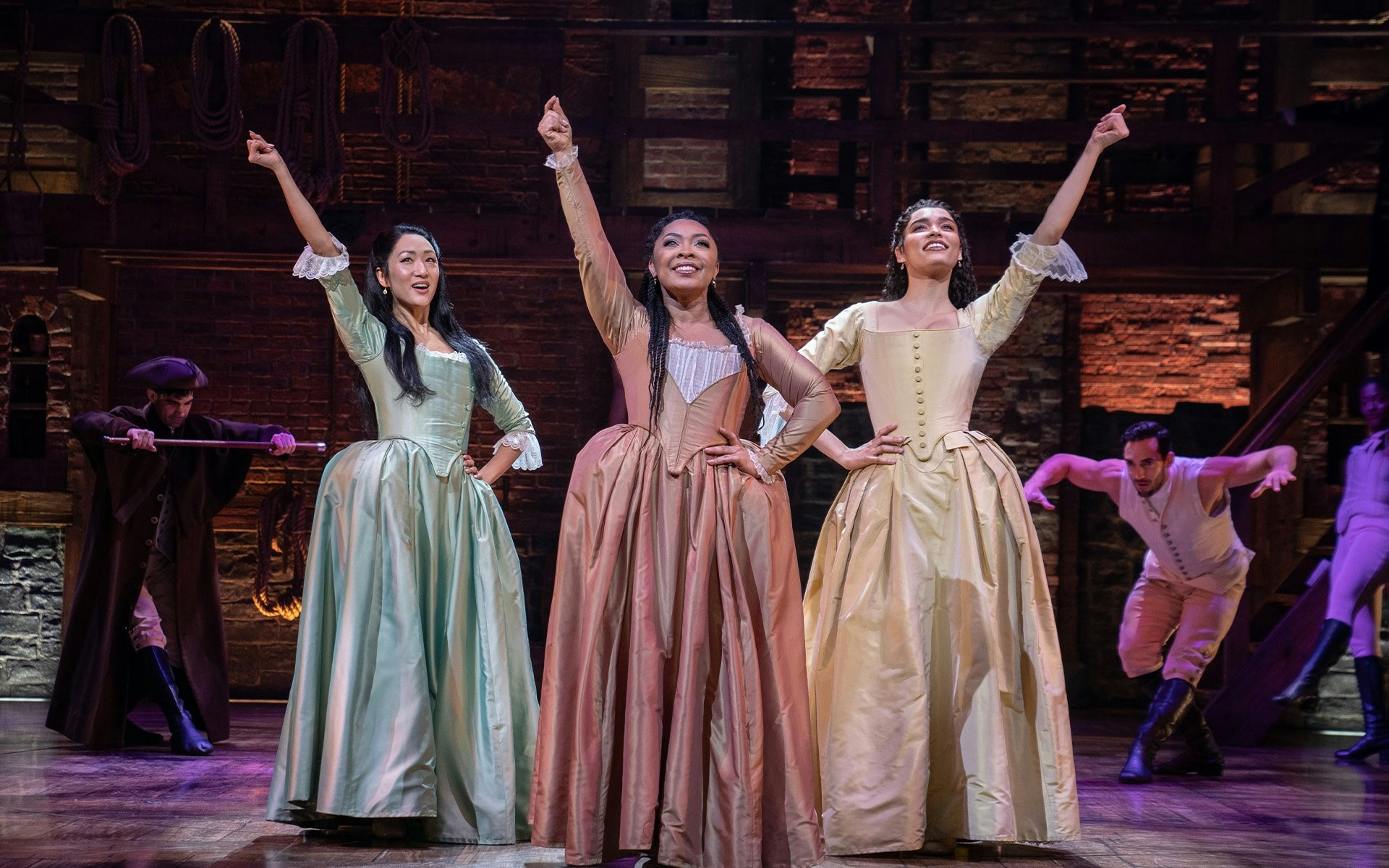 Performers in period costumes on stage during a scene from the musical Hamilton.
