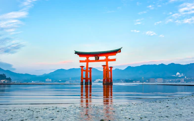 Torii gate at Itsukushima Shrine, Hiroshima, viewed from the water with mountains in the background.