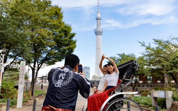 Tourist on rickshaw posing with Tokyo Skytree in background during Asakusa experience.