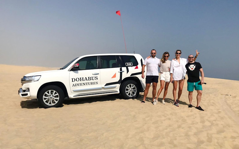 Group standing by a 4x4 vehicle on a desert safari in Doha.