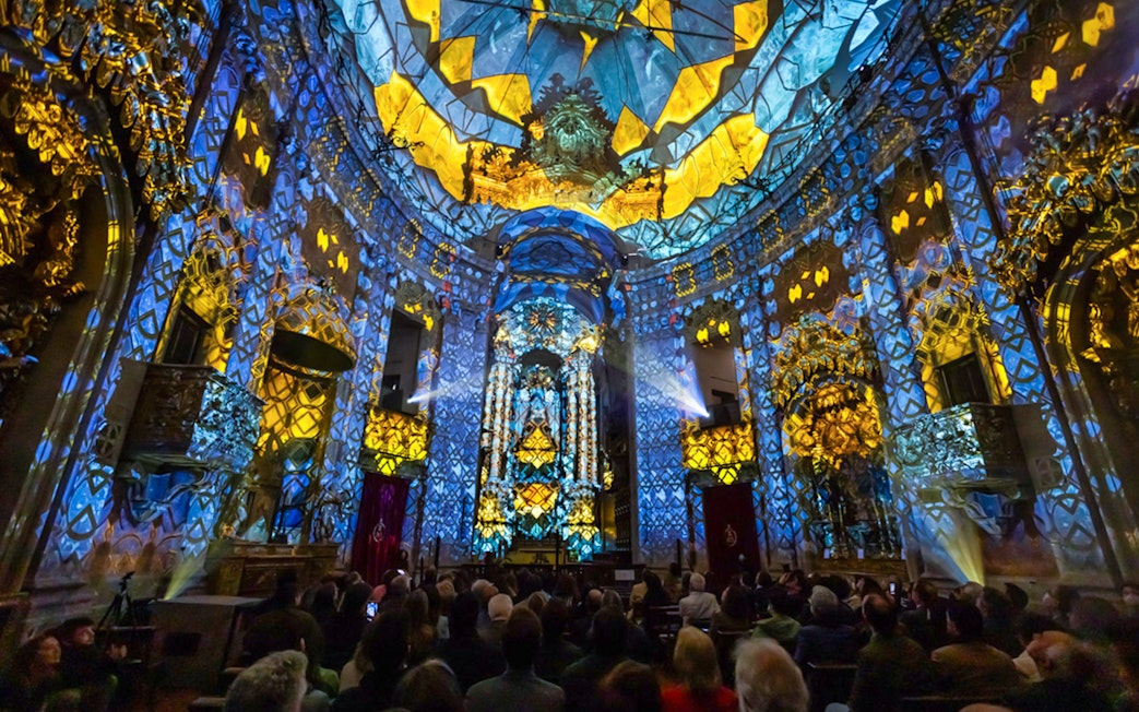 Light show at Clérigos Church, Porto, with audience watching vibrant blue and yellow projections.
