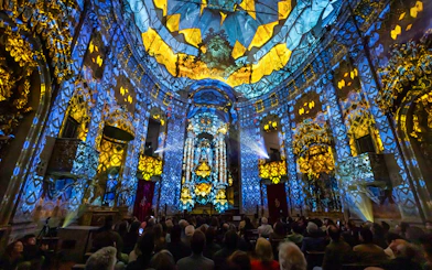 Light show at Clérigos Church, Porto, with audience watching vibrant blue and yellow projections.