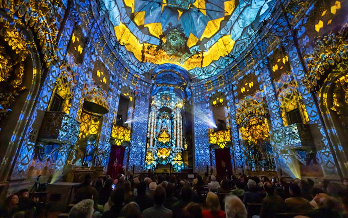 Light show at Clérigos Church, Porto, with audience watching vibrant blue and yellow projections.