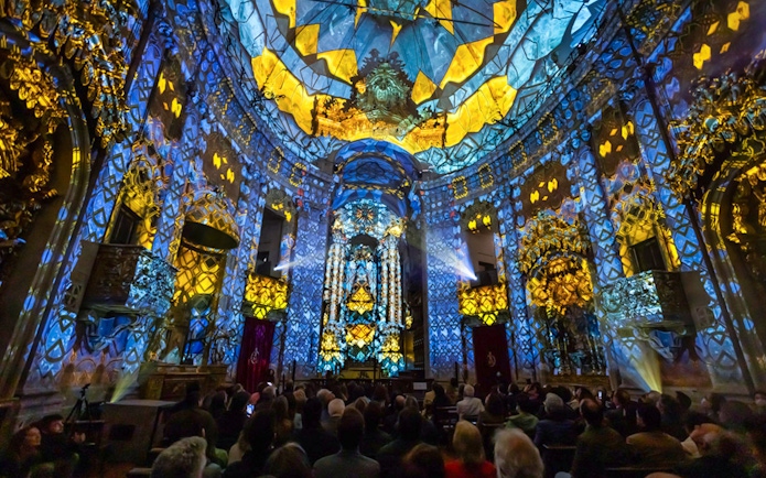 Light show at Clérigos Church, Porto, with audience watching vibrant blue and yellow projections.