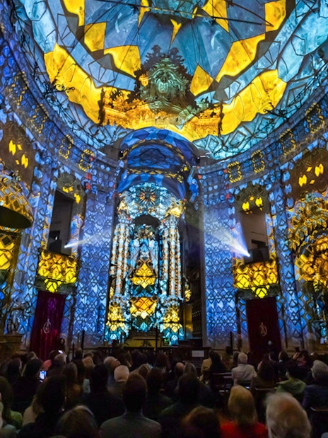 Light show at Clérigos Church, Porto, with audience watching vibrant blue and yellow projections.