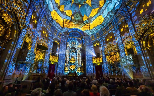 Light show at Clérigos Church, Porto, with audience watching vibrant blue and yellow projections.
