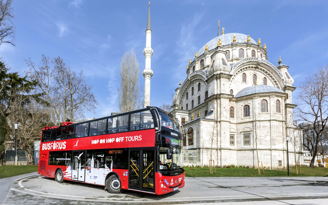 Red double-decker Busforus tour bus near Istanbul mosque, part of 1-day hop-on hop-off and Bosphorus cruise combo.