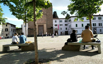 People sitting on benches in a sunny Florence square, Italy, near historic buildings.