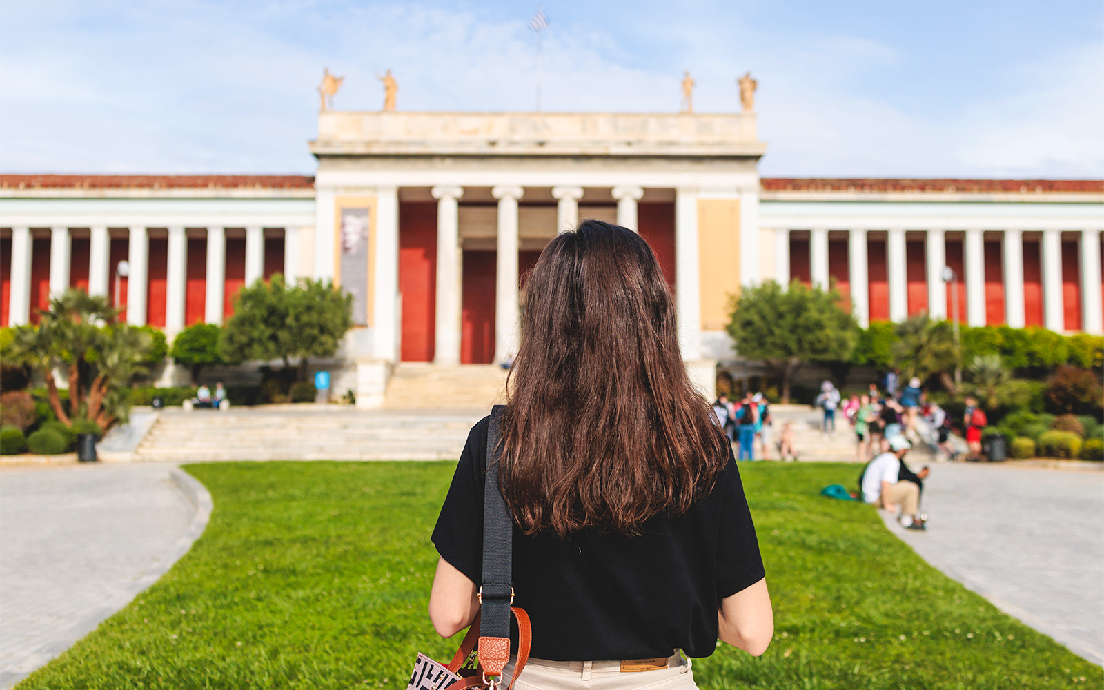 Woman staning in front of National Archaeological Museum entrance facade, Athens, Greece, showcasing neoclassical architecture.