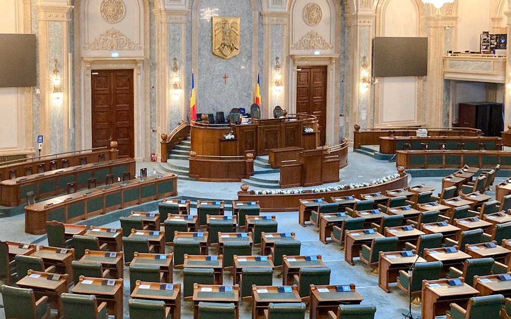 Parliament chamber with wooden desks and Romanian flags inside Palace of Parliament.