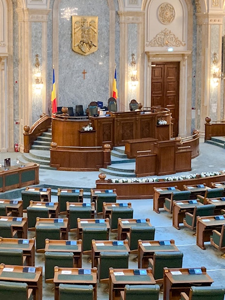 Parliament chamber with wooden desks and Romanian flags inside Palace of Parliament.
