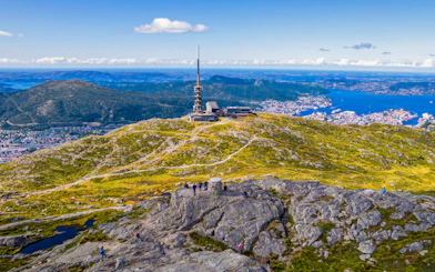 Ulriksmasten tower on Mount Ulriken with hikers and Bergen cityscape in the background.