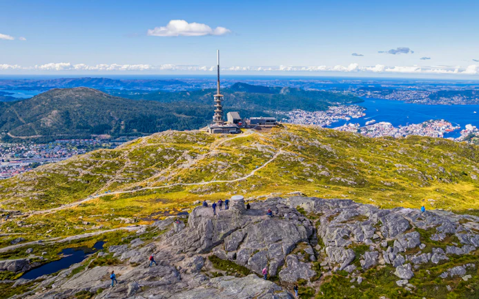Ulriksmasten tower on Mount Ulriken with hikers and Bergen cityscape in the background.