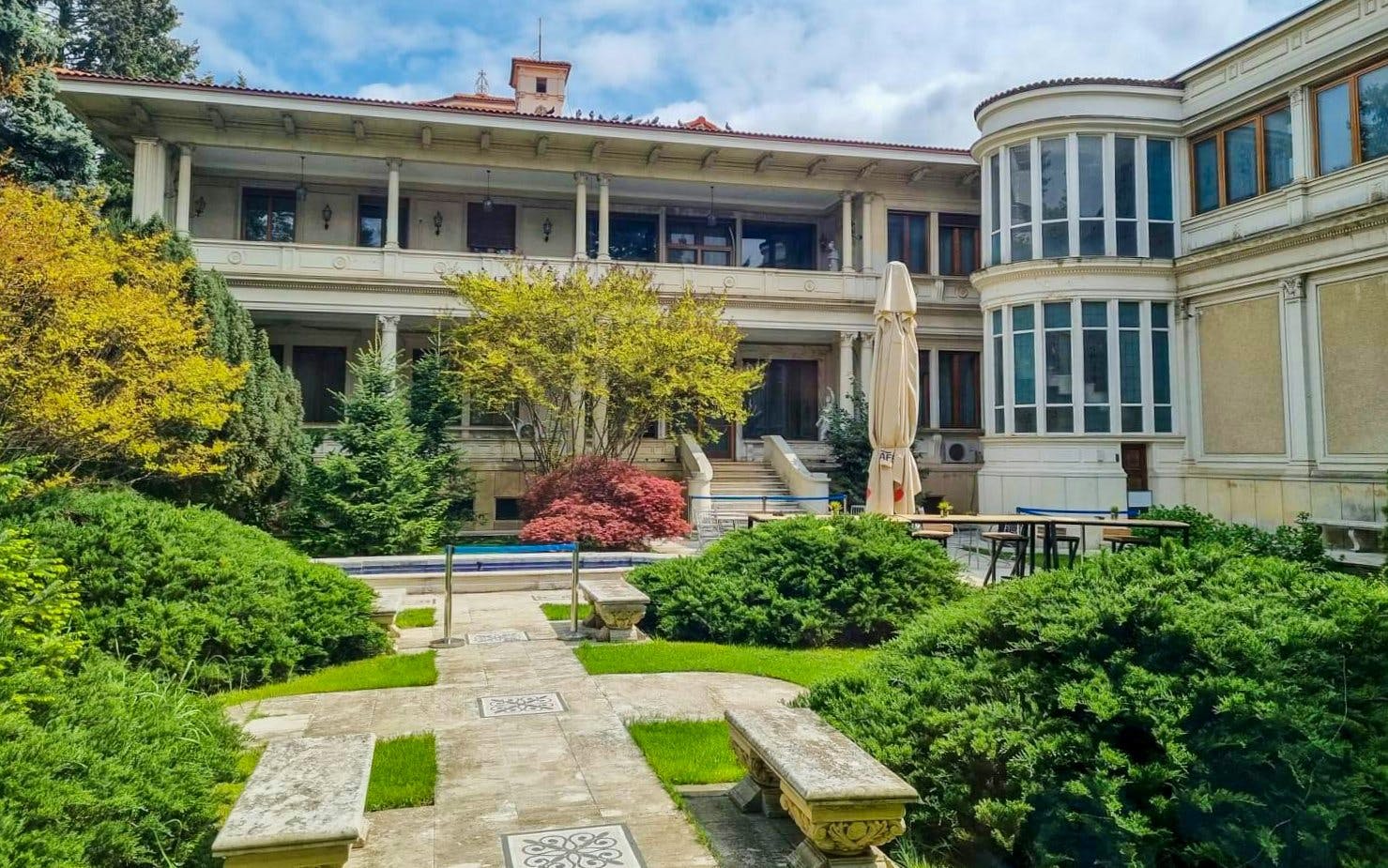 Courtyard of Ceausescu Mansion in Bucharest with lush greenery and historic architecture.