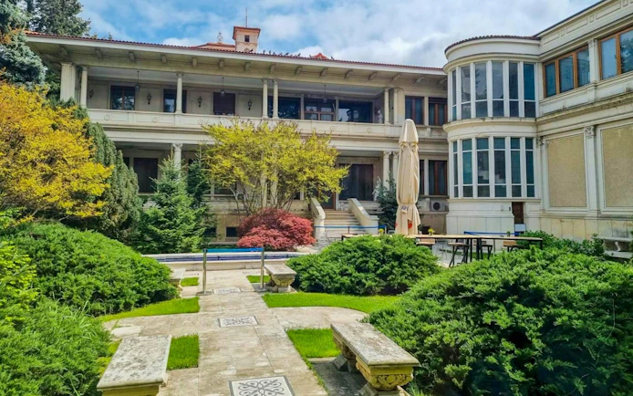 Courtyard of Ceausescu Mansion in Bucharest with lush greenery and historic architecture.